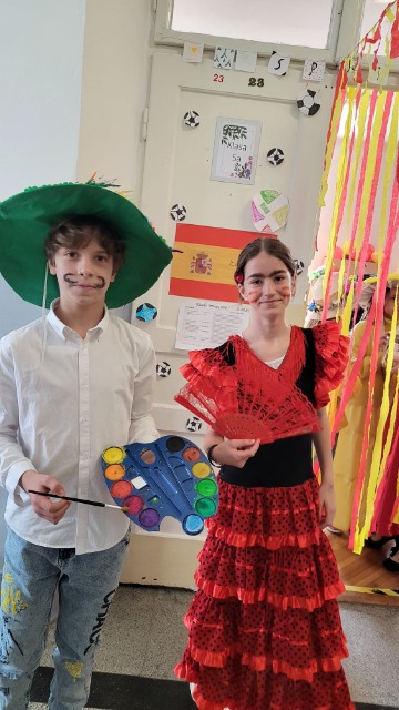 Dziecko przebrane za malarza i hiszpankę. Chłopiec ma na głowie zielony kapelusz. Ubrany w białą koszulę. W ręce trzyma paletę z farbami i pędzel. Z tyłu hiszpańska flaga.