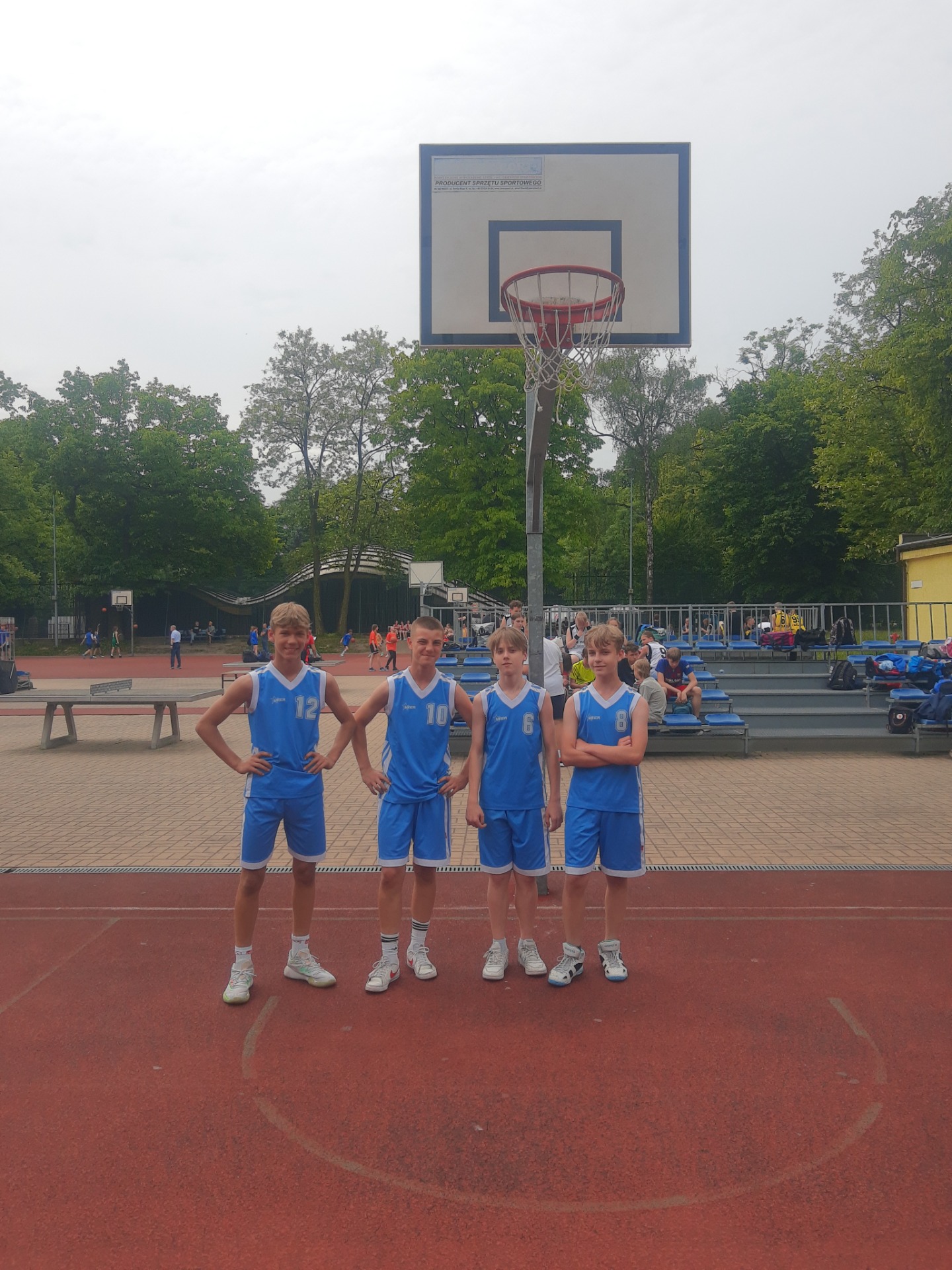 Trzech chłopców w sportowych niebieskich strojach na tle kosza do gry w koszykówkę.