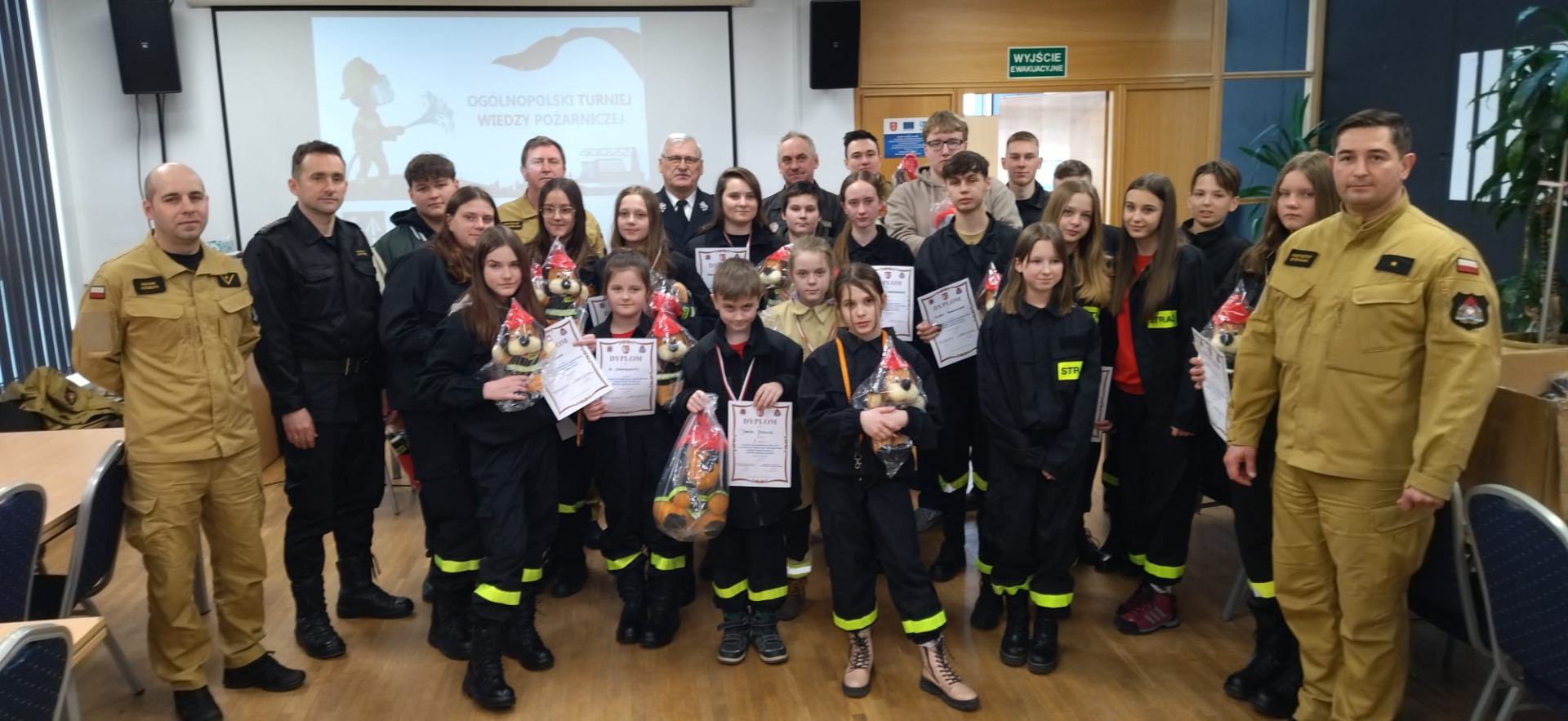 Liczna grupa młodzieży w strojach strażackich  z dyplomami i nagrodami oraz przedstawiciele organizatorów