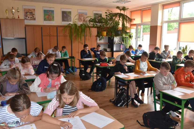 Uczniowie siedzą w ławkach i piszą test egzaminacyjny