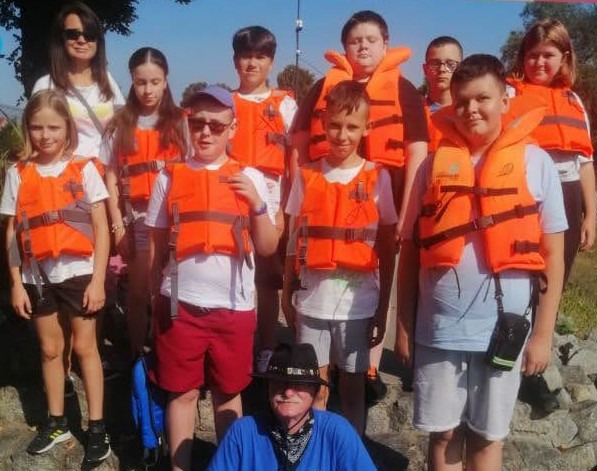 Grupowe zdjęcie klasy VI a z wychowawczynią i kapitanem statku - uczniowie w pomarańczowych kamizelkach ratunkowych