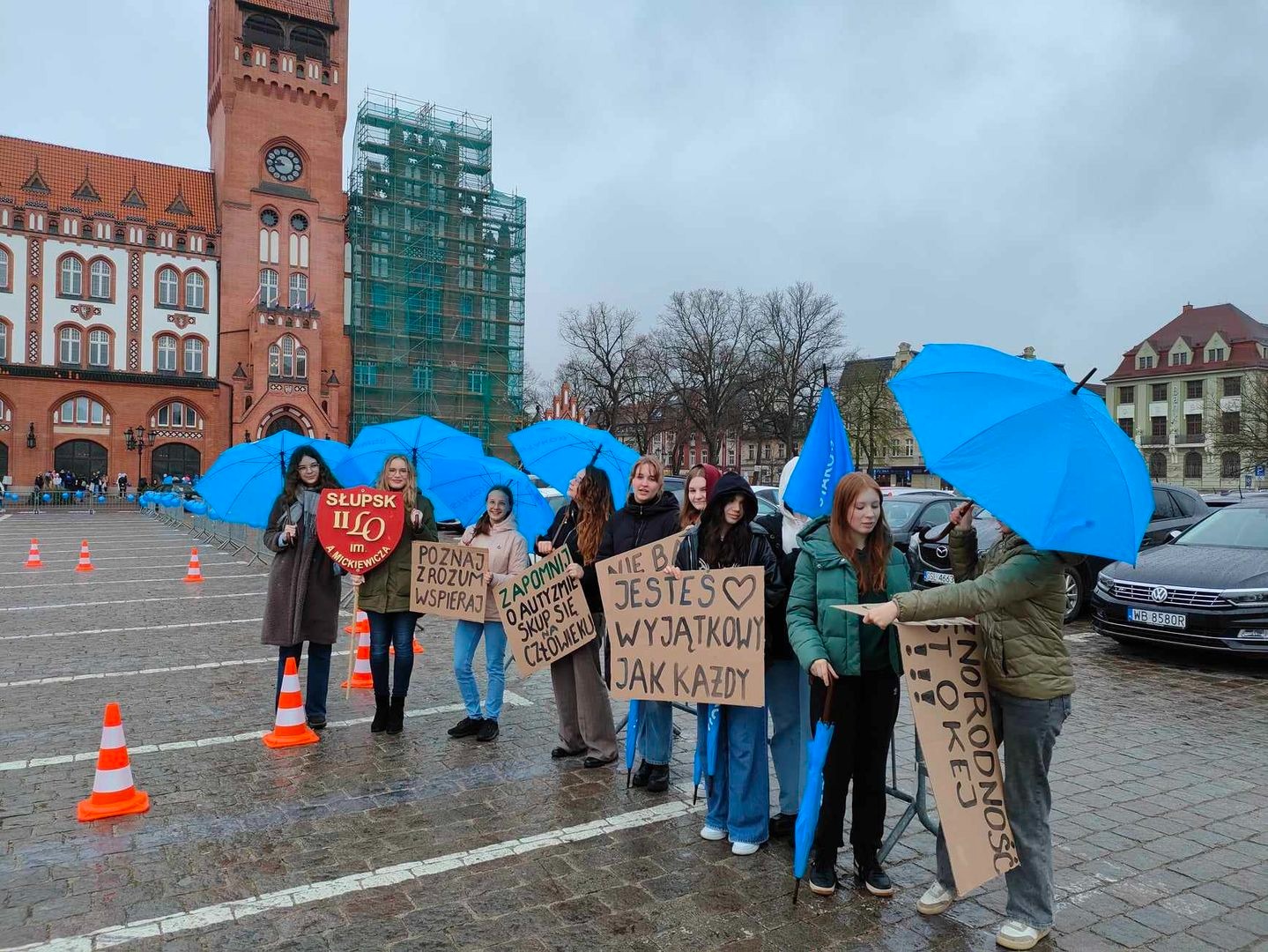 Uczennice na placu z niebieskimi parasolkami i plakatami