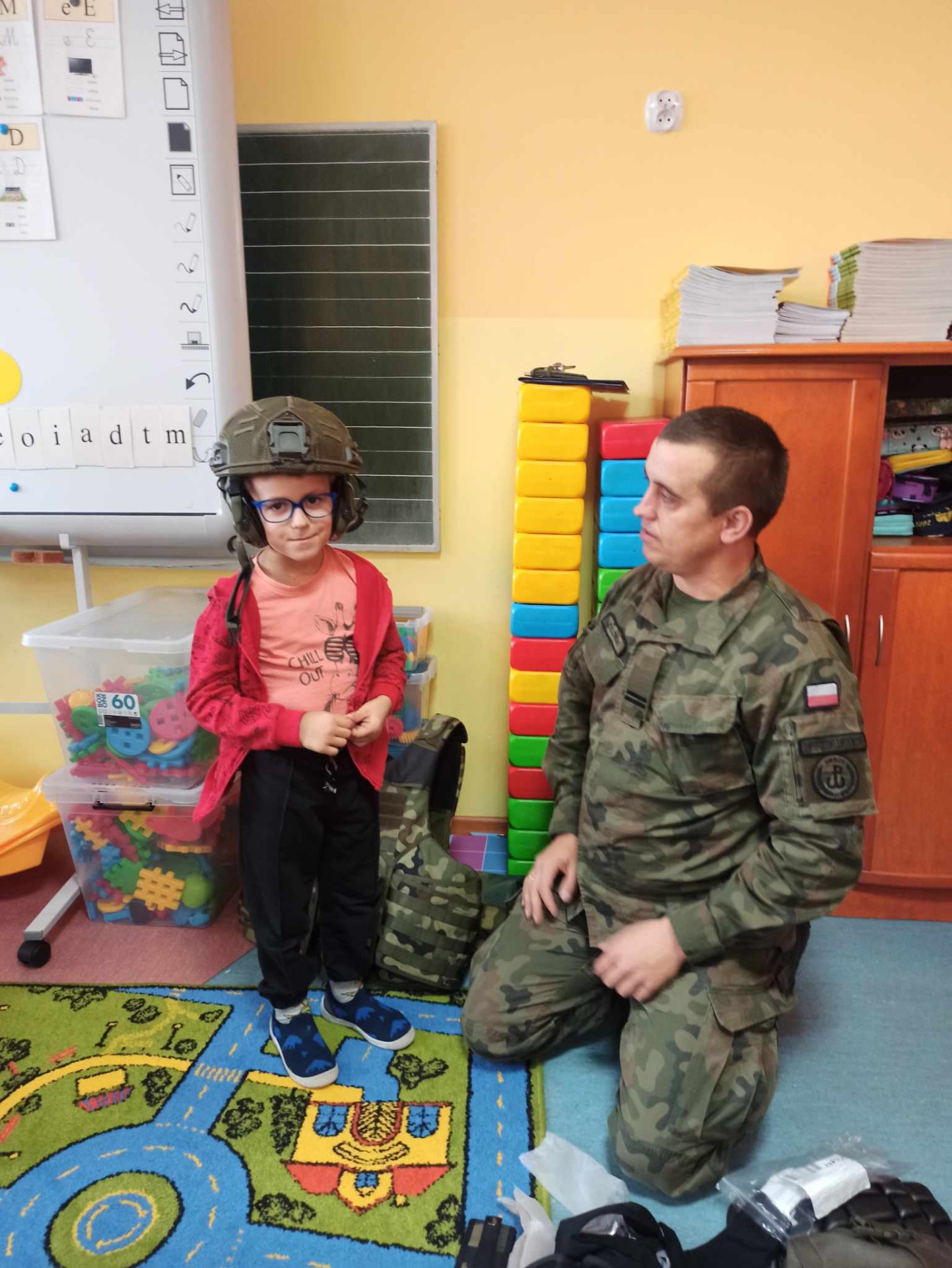Dzieci z oddziałów przedszkolnych przymierzają hełm wojskowy.
