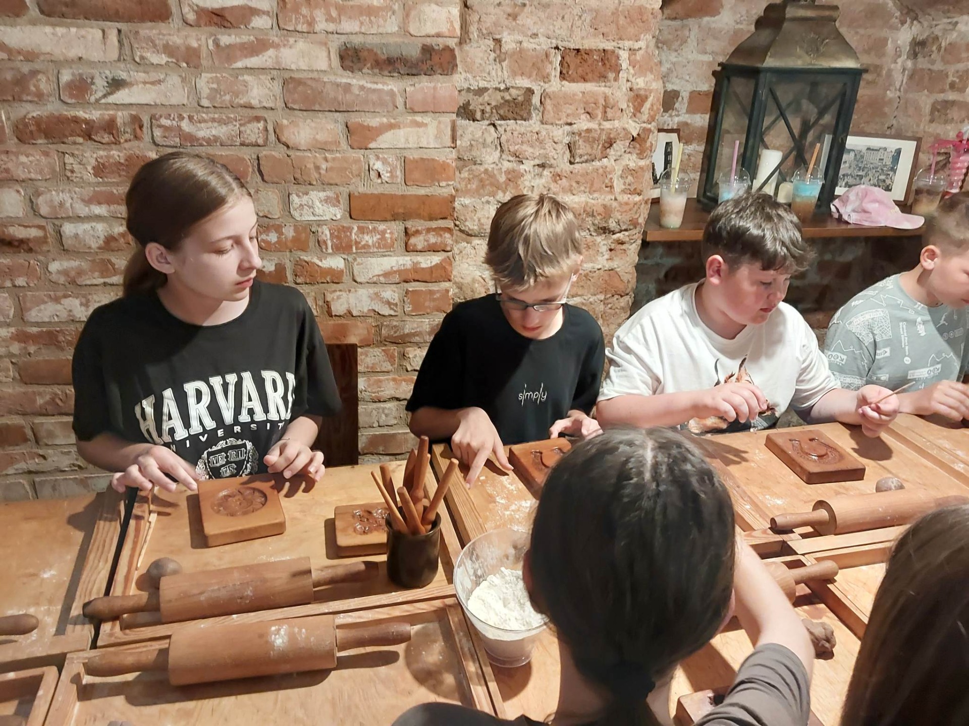 Grupa uczniów siedzi przy drewnianym stole w czasie warsztatów wyrabiani piernika