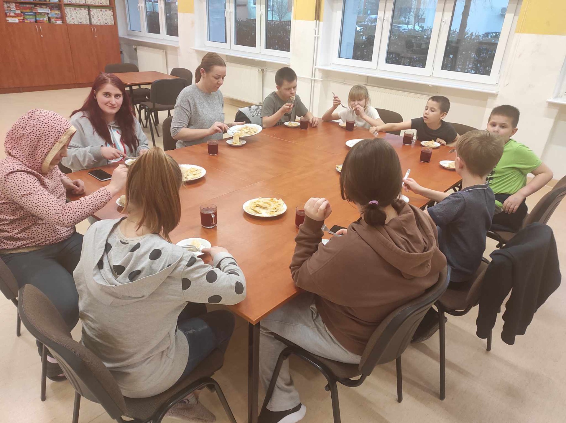 Grupa dzieci z wychowawczyniami wspólnie siedzi przy stole i je pierogi z serem.