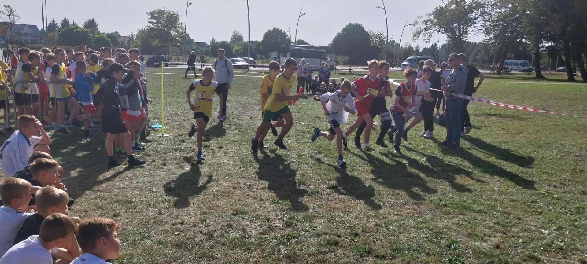 Grupa uczniów biegnie w sztafetowych biegach przełajowych
